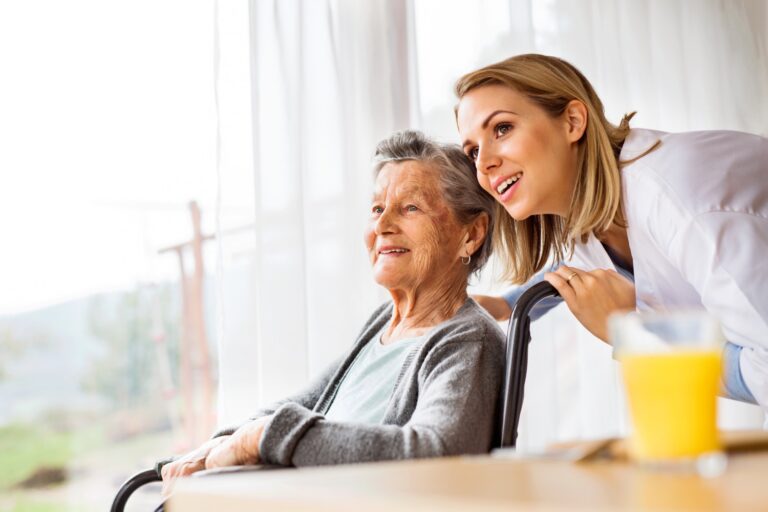 A live-in caregiver helps her elderly client look out a window.