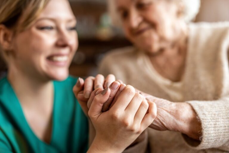 Elderly woman and young caretaker holding hands and smiling.